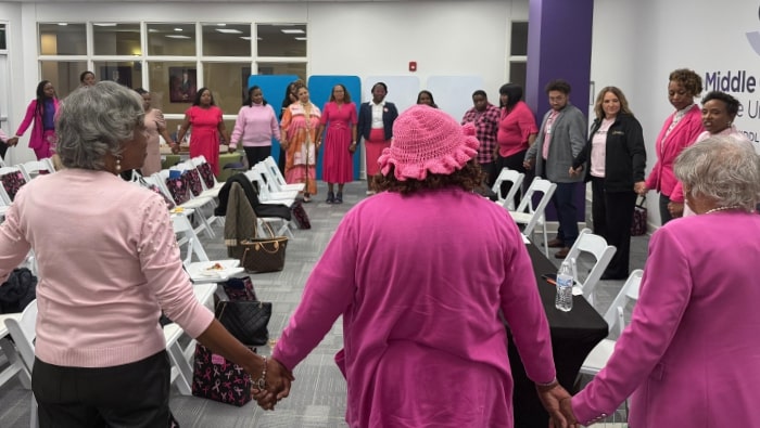 A crowd of attendees wearing pink and holding hands in a circle at the CMGS